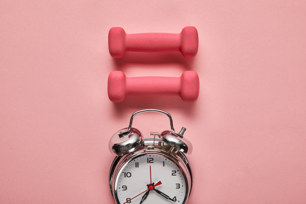 flat lay with silver alarm clock and pink dumbbells on pink background - Foto, Imagem