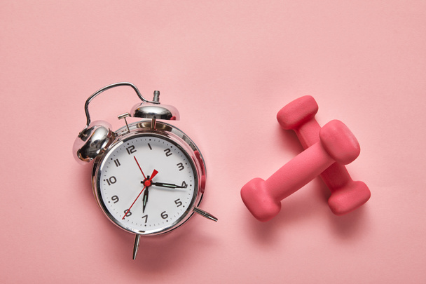 top view of silver alarm clock and pink dumbbells on pink background - Φωτογραφία, εικόνα