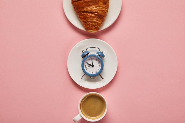 flat lay with coffee cup, toy alarm clock and croissant on plate on pink background - Photo, Image