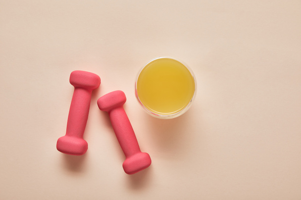 top view of pink dumbbells, orange juice on beige background - Φωτογραφία, εικόνα