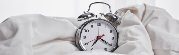 panoramic shot of silver alarm clock covered with blanket in white bed  - Foto, Imagen