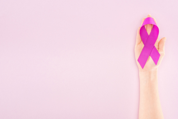 περικομμένη όψη της μωβ κορδέλας στο χέρι της γυναίκας που απομονώνεται σε ροζ - Φωτογραφία, εικόνα