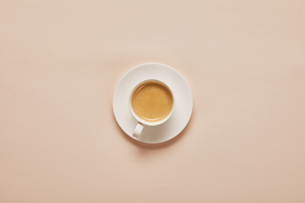 top view of coffee in cup on saucer on beige background - Foto, Imagem
