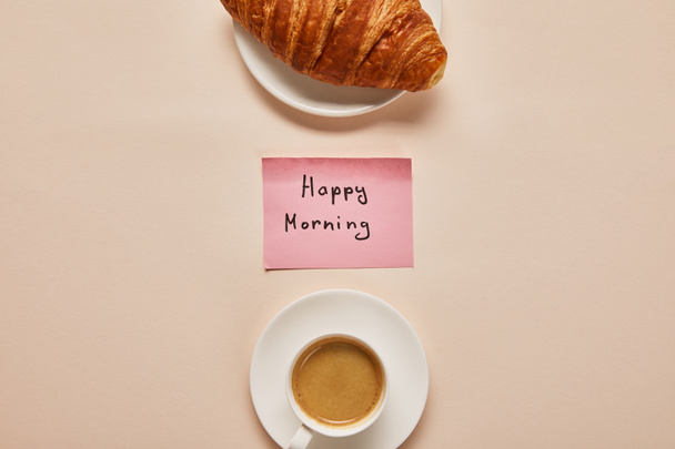 flat lay with coffee, croissant and sticky note with happy morning lettering on beige background - Foto, Imagem