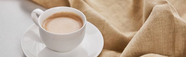 close up view of coffee in white cup on saucer near beige napkin, panoramic shot - 写真・画像