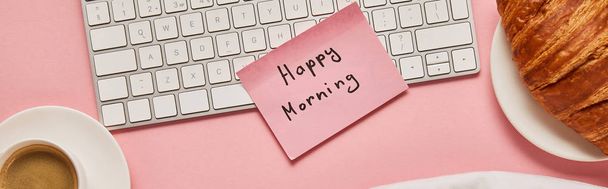 вид сверху на клавиатуру компьютера и розовую липкую ноту с радостными утренними надписями возле круассана и кофе на розовом фоне, панорамный снимок
 - Фото, изображение