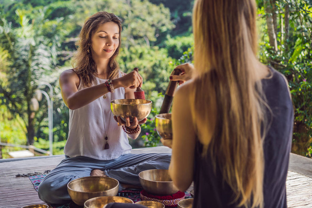 Nepal Buddha copper singing bowl at spa salon. Young beautiful woman doing massage therapy singing bowls in the Spa against a waterfall. Sound therapy, recreation, meditation, healthy lifestyle and - Photo, image