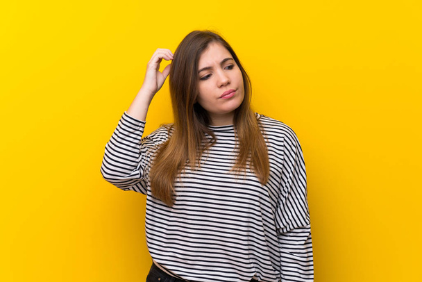 Young girl over yellow wall having doubts while scratching head - Photo, Image