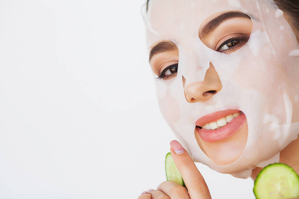 Hermosa joven mujer está recibiendo máscara de arcilla facial en el spa, acostado con pepinos en los ojos
 - Foto, Imagen