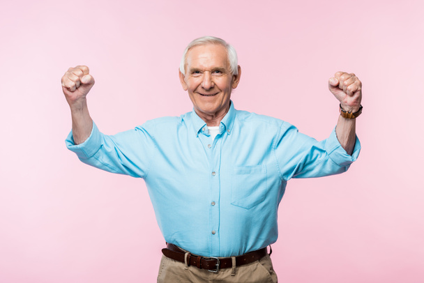 χαρούμενος συνταξιούχος άνθρωπος δείχνοντας γροθιές και χαμογελά σε ροζ  - Φωτογραφία, εικόνα