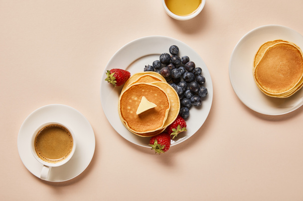 top view of pancakes with berries, near cup of coffee and bowl with honey on pink  - Фото, изображение