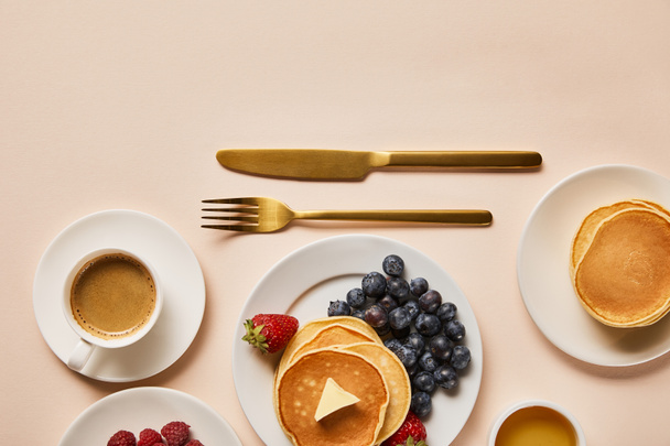 vista superior del delicioso desayuno servido con panqueques, bayas, miel y café cerca de cubiertos de oro
 - Foto, Imagen