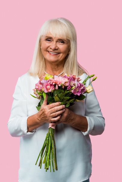 happy senior woman standing with bouquet of blooming flowers isolated on pink  - Photo, image