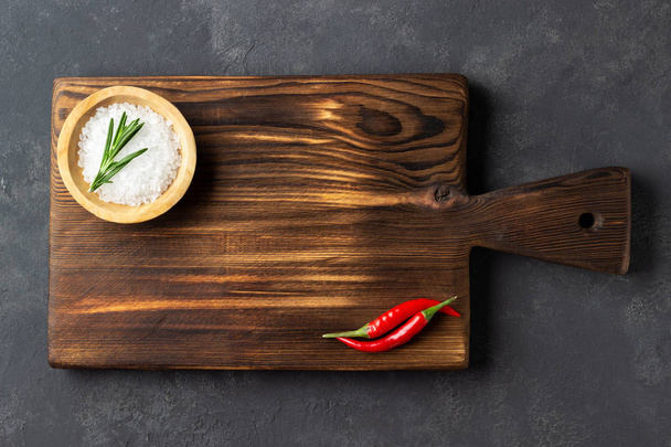 Cooking concept. Vintage cutting board with salt  and red pepper on dark stone background. Copy space. - Foto, Imagem