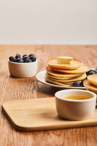 selektiver Fokus von Pfannkuchen mit Butter, Blaubeeren und Honig auf Holzoberfläche isoliert auf grau  - Foto, Bild