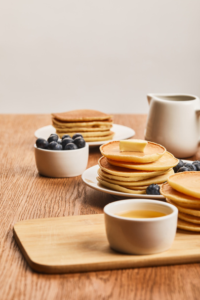 selective focus of plates with pancakes, berries, honey in bowl and syrup in jug isolated on grey - Valokuva, kuva