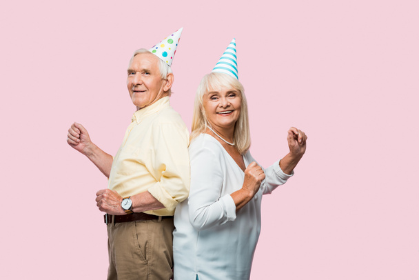 веселий старший чоловік і дружина в партійних шапках жестикулюють ізольовані на рожевому
  - Фото, зображення