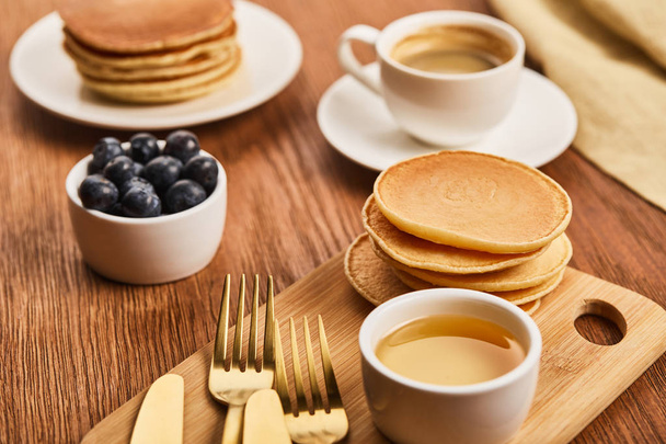 selective focus of pancakes near bowl with honey and blueberries, golden cutlery and cup of coffee - Foto, Imagem