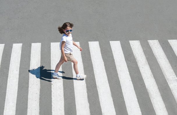 In the summer on the street at the pedestrian crossing kid girl in fashion clothes cross the road. From top view. Shadow at zebra crossing - Foto, Bild