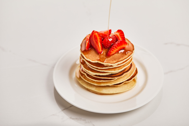 pouring syrup on tasty pancakes with strawberries on white plate on textured surface - Photo, image