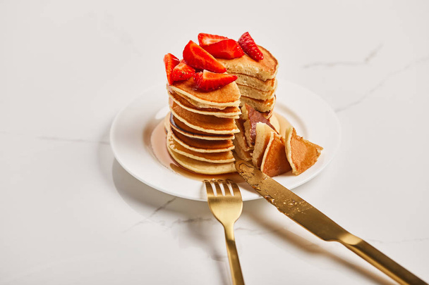 golden cutlery on plate with slice of pancakes with strawberries on textured surface - Photo, Image