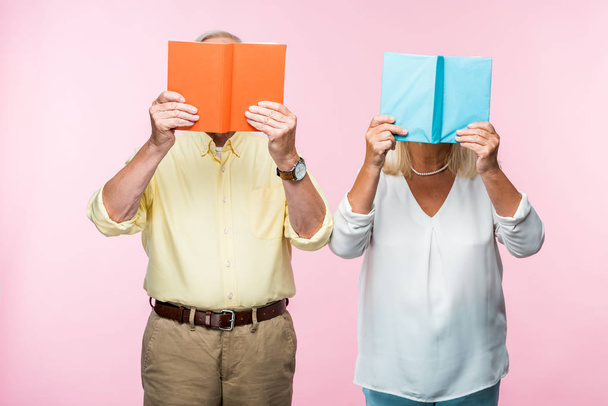ピンクで隔離された本で顔を覆う年金生活者のカップル  - 写真・画像