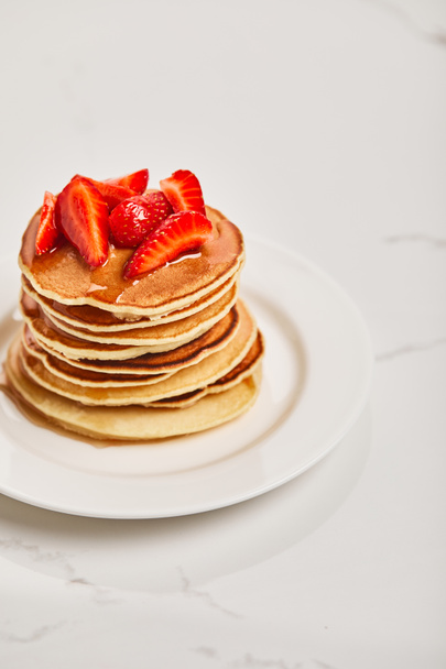 pancakes with strawberries and syrup on white plate on textured surface - Photo, Image