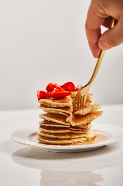 cropped view of man taking slice of pancakes with strawberries on white plate isolated on grey - Photo, Image