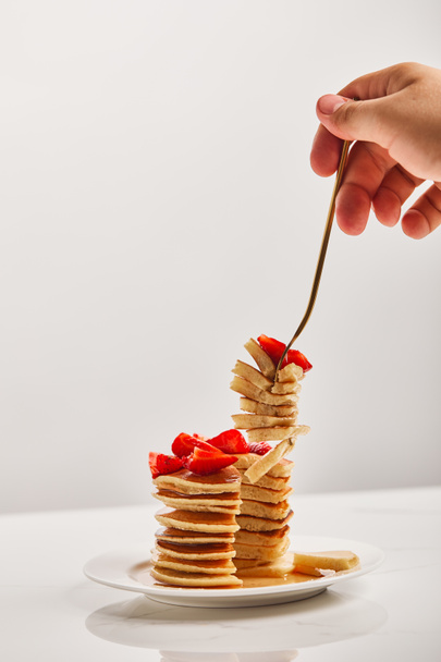cropped view of man taking slice of pancakes with golden fork from white plate  - Foto, immagini