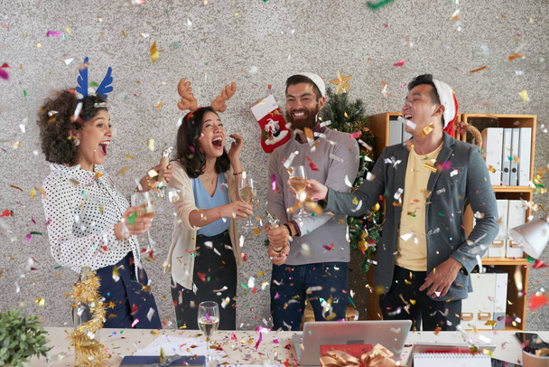 Laughing happy multi-ethnic coworkers drinking champagne under falling confetti - Foto, Imagen
