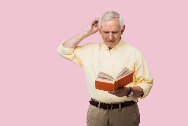 pensive senior man touching grey hair and reading book isolated on pink  - Foto, Bild