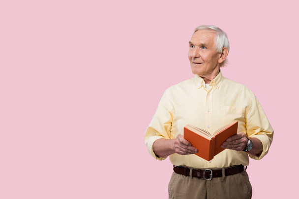 Gelukkig gepensioneerde man Holding boek en glimlachend geïsoleerd op roze  - Foto, afbeelding