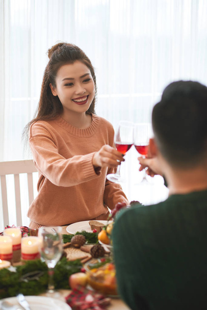 美しい若いベトナムの女性と彼女のボーイフレンドは、クリスマスのディナーテーブルでワインを飲みます - 写真・画像