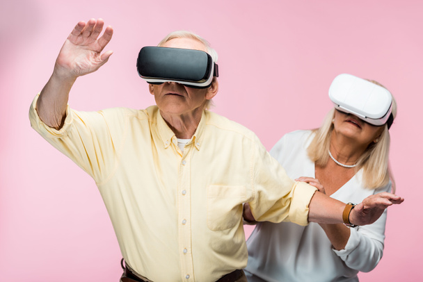 Rentner gestikuliert mit Virtual-Reality-Headset neben Frau auf rosa  - Foto, Bild