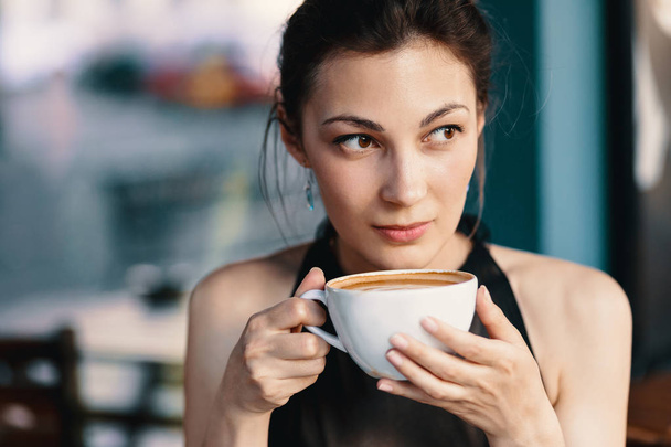 Verfijnde vrouw genieten van cappuccino of Latte op een levendige, kleurrijke achtergrond binnenshuis. - Foto, afbeelding