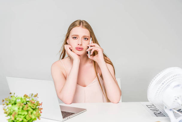 beautiful girl talking on smartphone and suffering from heat at computer desk isolated on grey - Photo, Image