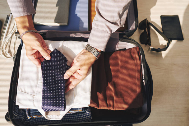 Empresario poniendo corbata y otra ropa en maletín, vista desde arriba
 - Foto, Imagen