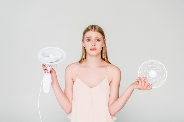hermosa mujer joven confundida sosteniendo ventilador eléctrico aislado en gris
 - Foto, imagen