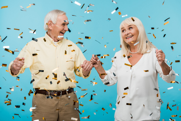 feliz jubilado marido y esposa cerca de caer confeti en azul
  - Foto, Imagen