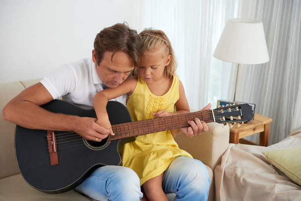 Молодий чоловік показує доньці, як грати на гітарі
 - Фото, зображення