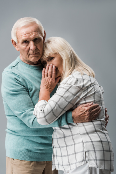 sad retired man hugging frustrated senior wife covering face isolated on grey  - Foto, Imagen