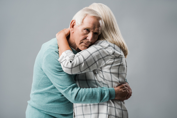 sad retired man hugging senior wife and looking at camera isolated on grey  - Fotoğraf, Görsel