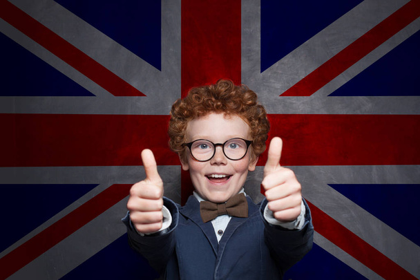Boldog gyermek fiú mutató hüvelykujját ellen az Egyesült Királyság zászló háttérben. - Fotó, kép
