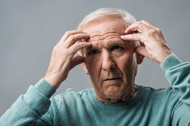 exhausted retired man looking at camera and touching head isolated on grey  - Foto, Imagen