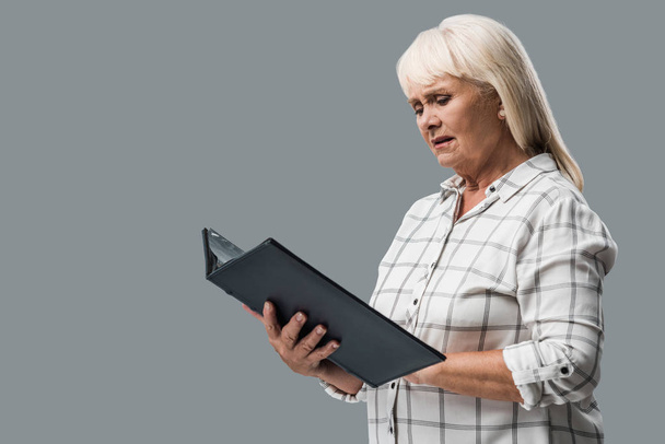 upset retired woman looking at photo album isolated on grey  - Zdjęcie, obraz