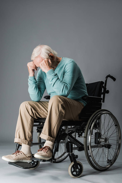  jubilado sentado en silla de ruedas y cubriendo la cara en gris
 - Foto, imagen
