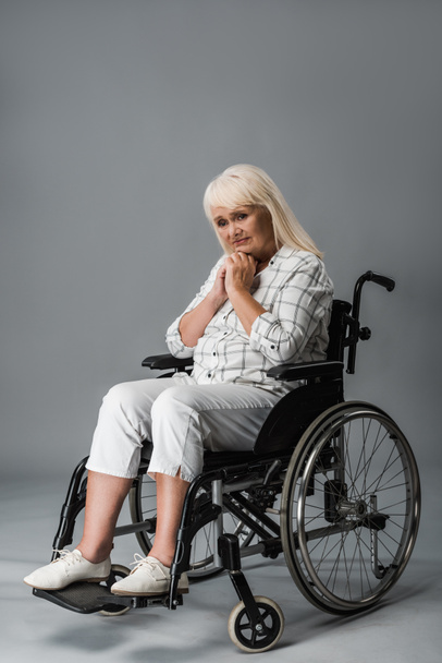 upset retired woman with clenched hands sitting in wheelchair on grey - Photo, Image