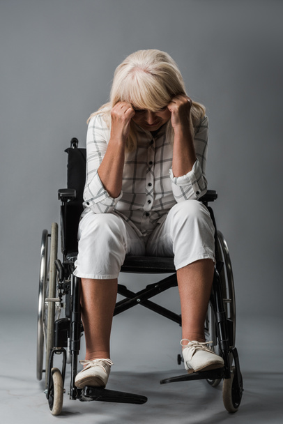 upset retired woman sitting in wheelchair and touching head on grey - 写真・画像