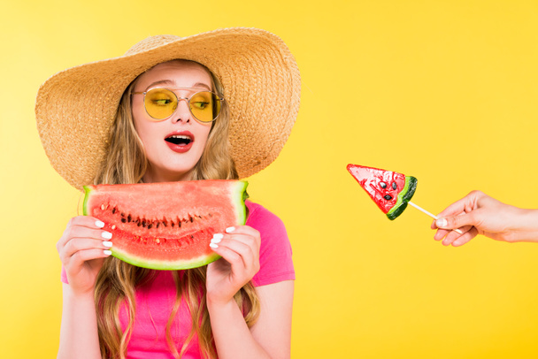 beautiful surprised girl in Straw Hat with watermelon looking at lollipop Isolated On yellow  - 写真・画像