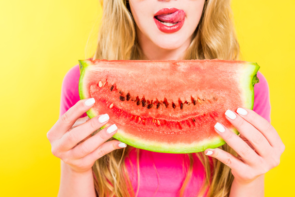abgeschnittene Ansicht des Mädchens, das die Zunge herausstreckt und Wassermelone isoliert auf gelb hält - Foto, Bild
